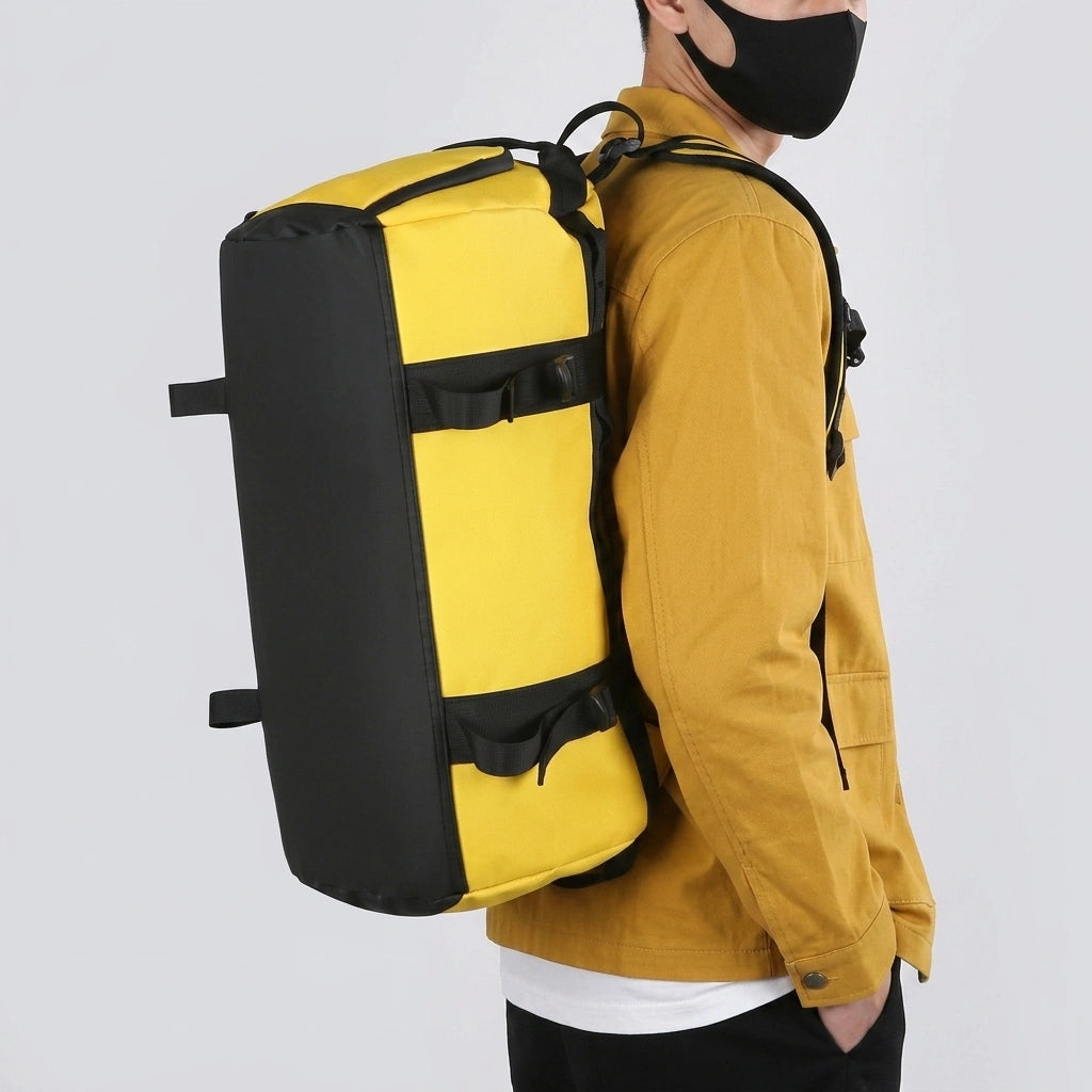 Homme portant le sac de voyage jaune en mode sac à dos avec bretelles, veste moutarde et masque noir