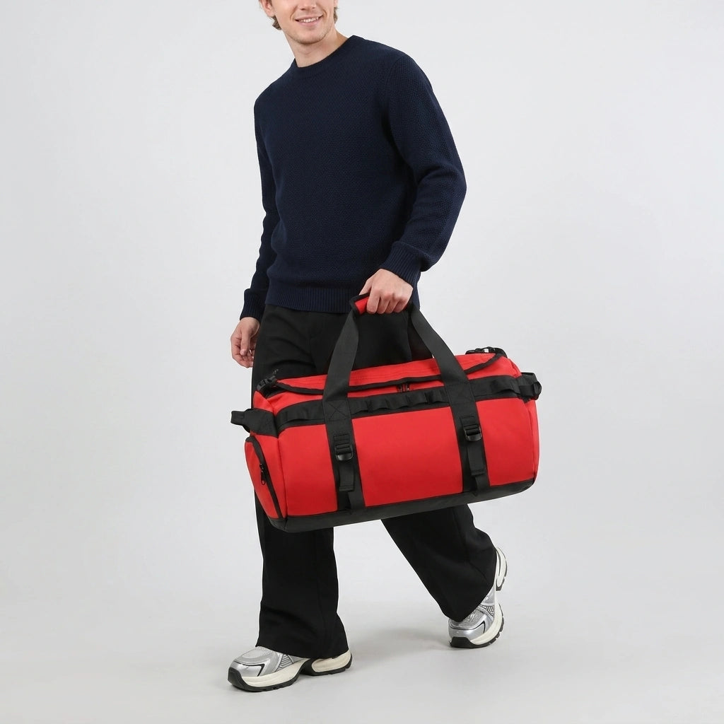 Homme en pull bleu marine portant le sac de voyage duffle rouge à la main en marchant sur fond studio