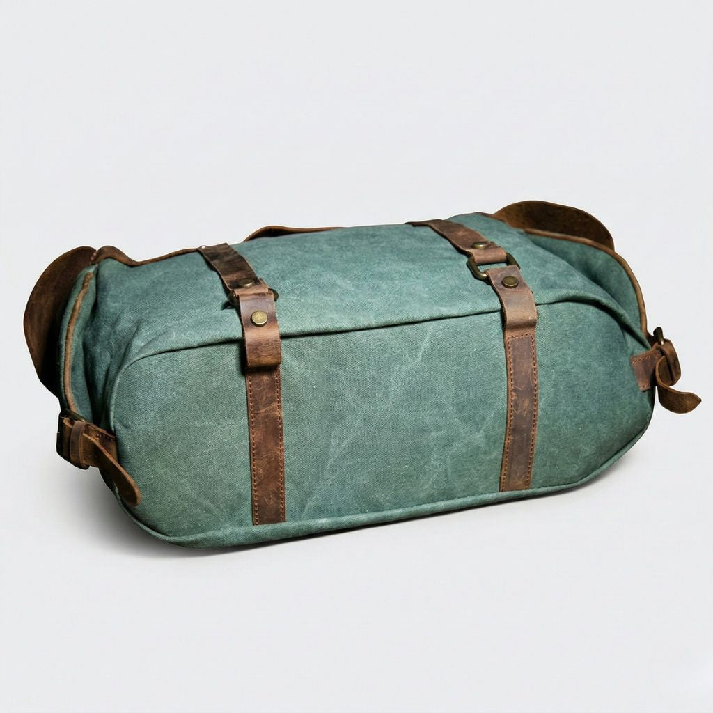 Sac de voyage vert forêt posé à plat : sangles cuir croisées avec rivets laiton et base cuir renforcée