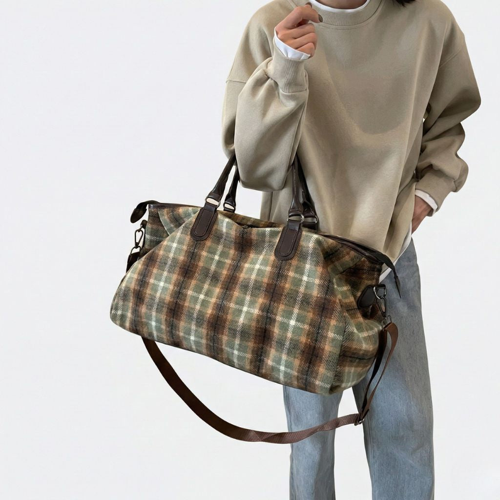 Femme portant sur l'épaule un sac de voyage en toile à carreaux tartan vert et marron, poignées cuir