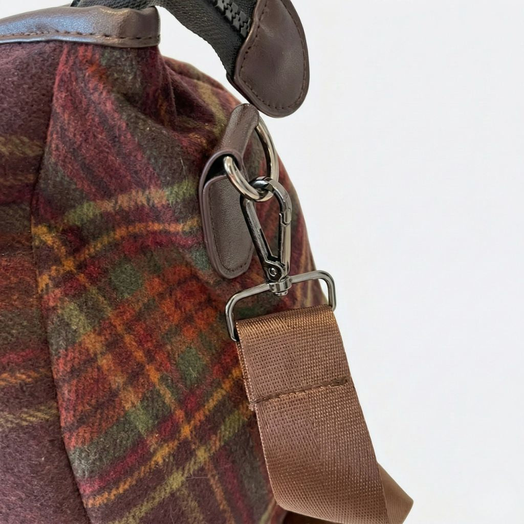 Détail du mousqueton de bandoulière du sac de voyage en toile tartan bordeaux, anneau et sangle en cuir brun