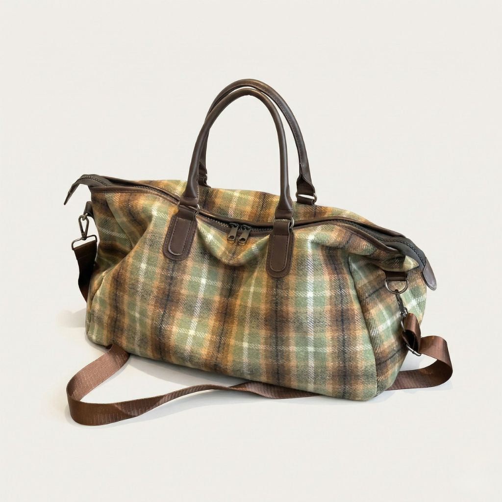 Sac de voyage en toile tartan kaki posé de face, poignées cuir brun, bandoulière et compartiment principal zippé
