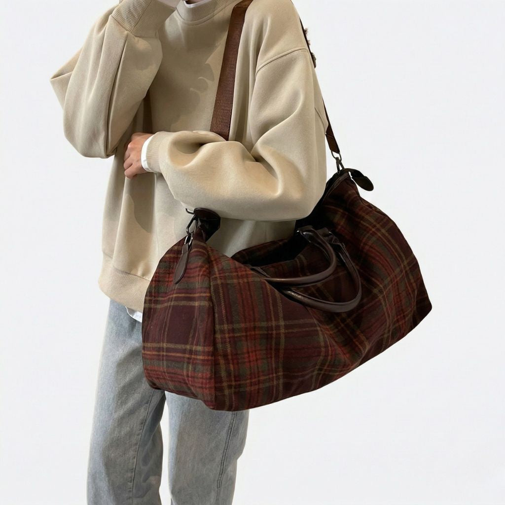 Personne portant sur l'épaule un sac de voyage en toile à carreaux tartan rouge et vert avec bandoulière