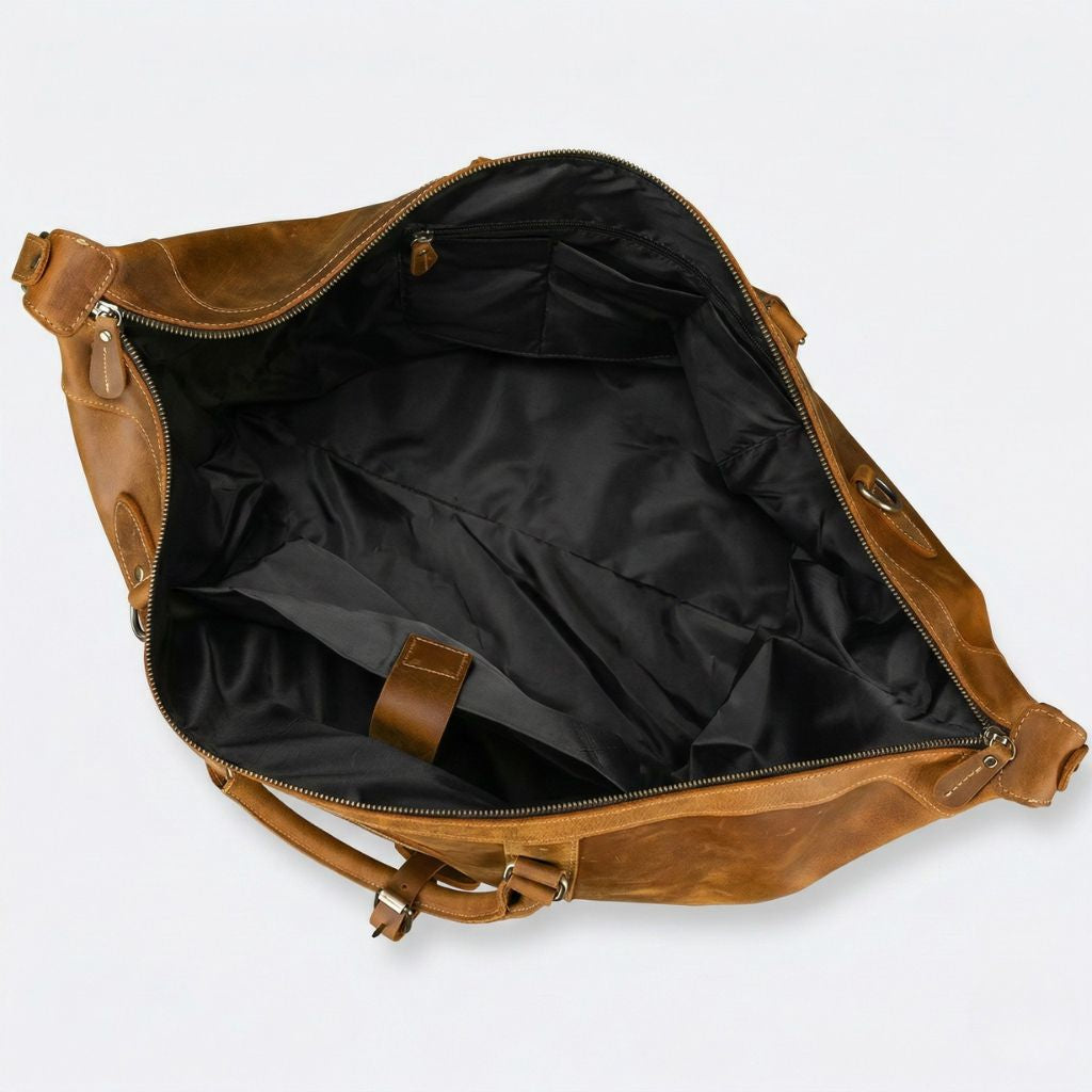 Vue aérienne du compartiment vide, doublure nylon noire, poche interne zippée et languette cuir caramel