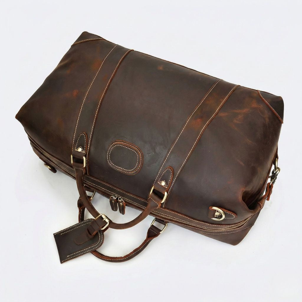Vue plongeante trois-quarts du sac cuir marron foncé, double fermeture zippée et étiquette bagage laiton