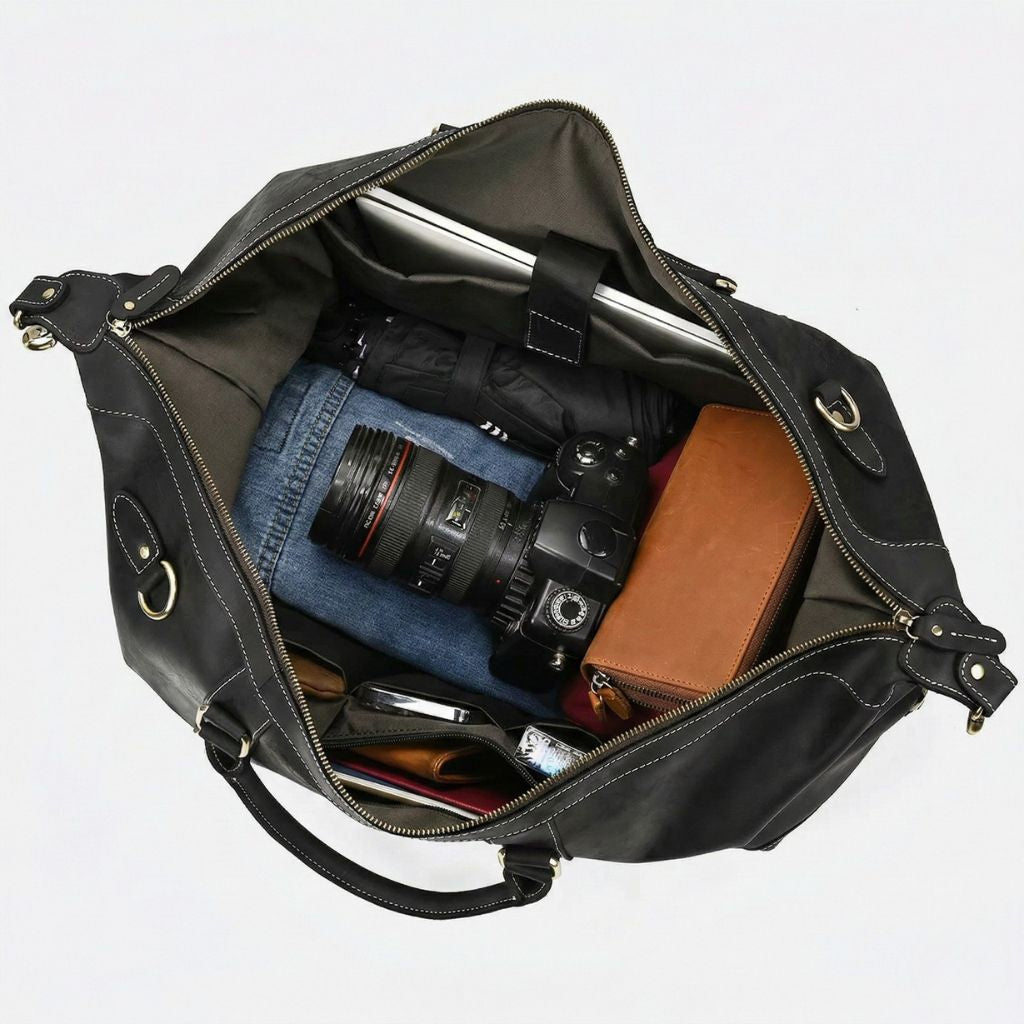 Compartiment principal ouvert du sac noir mat, jean, appareil photo reflex et pochette cognac sur doublure