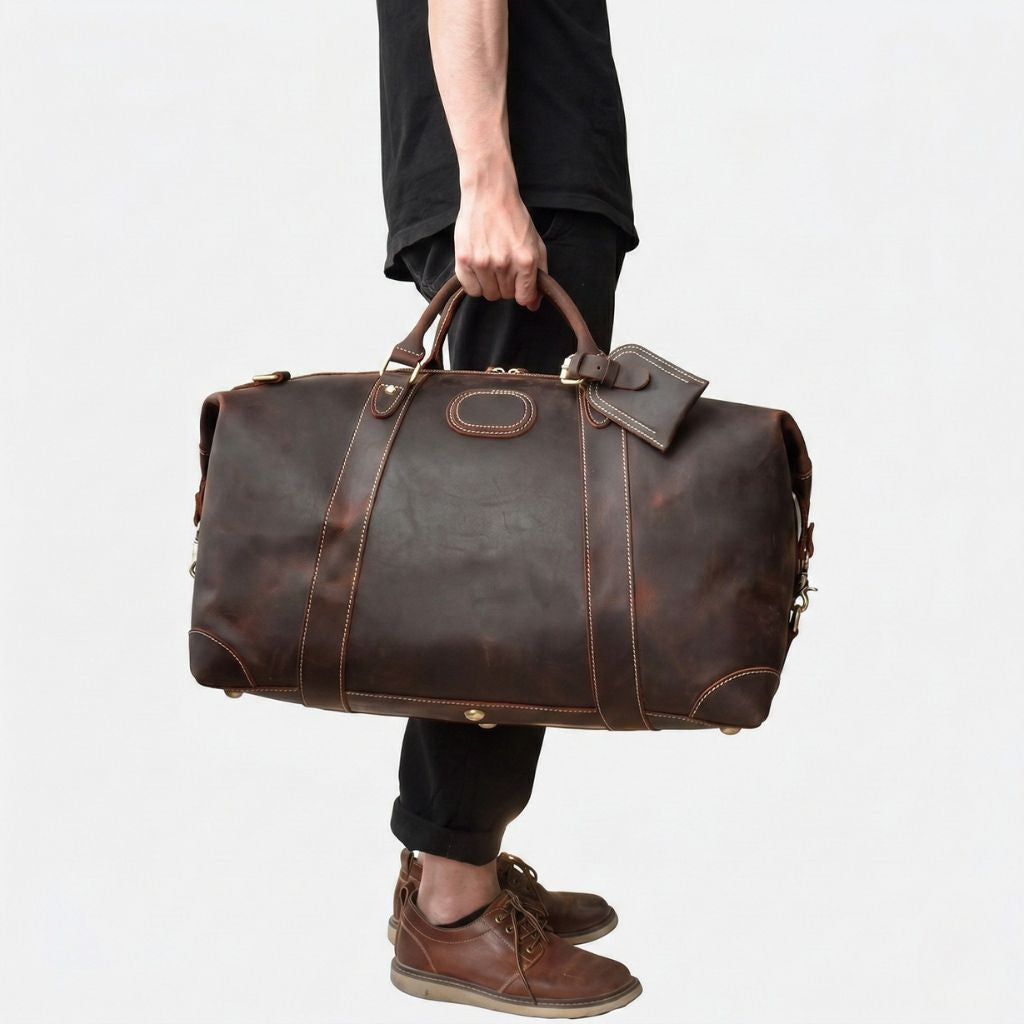 Homme tenant à la main le sac de voyage en cuir marron foncé, face avant et patine naturelle du cuir