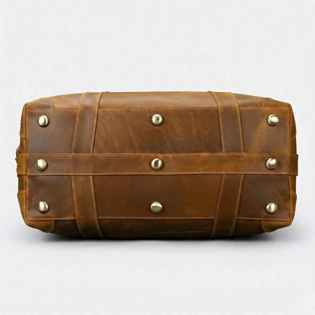 Fond du sac de voyage en cuir cognac, huit pieds protecteurs en laiton doré et coutures apparentes croisées