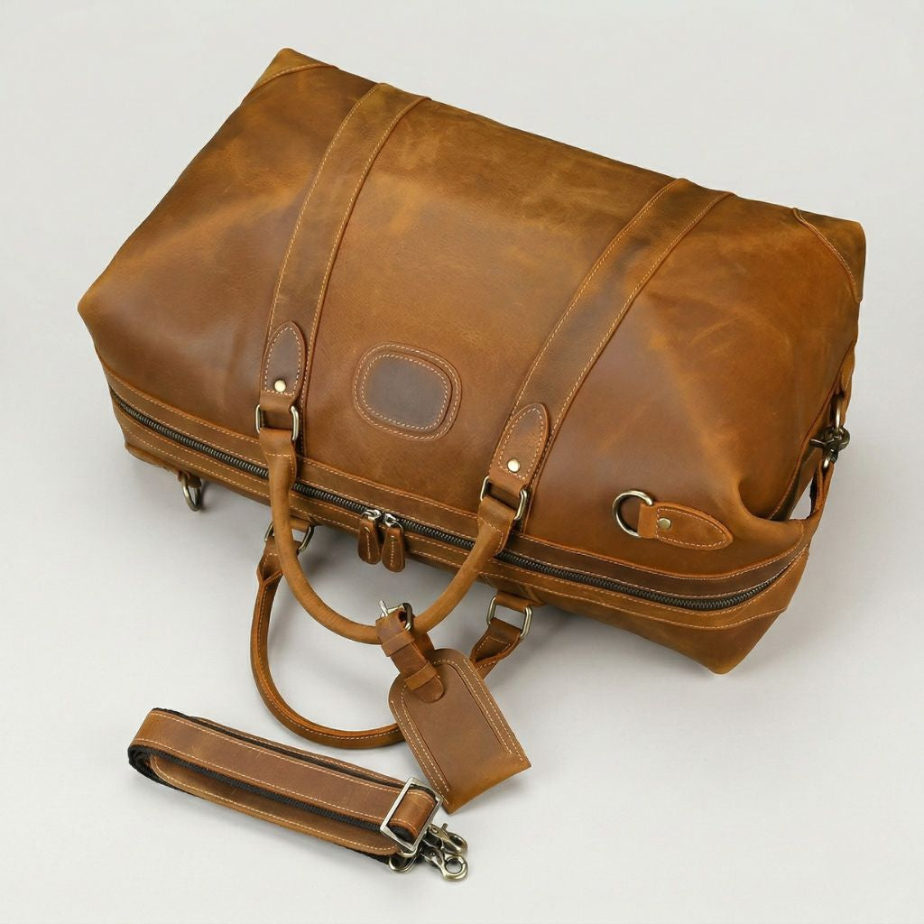 Vue plongeante du sac de voyage cuir caramel patiné, dos et bandoulière détachée posée sur la surface
