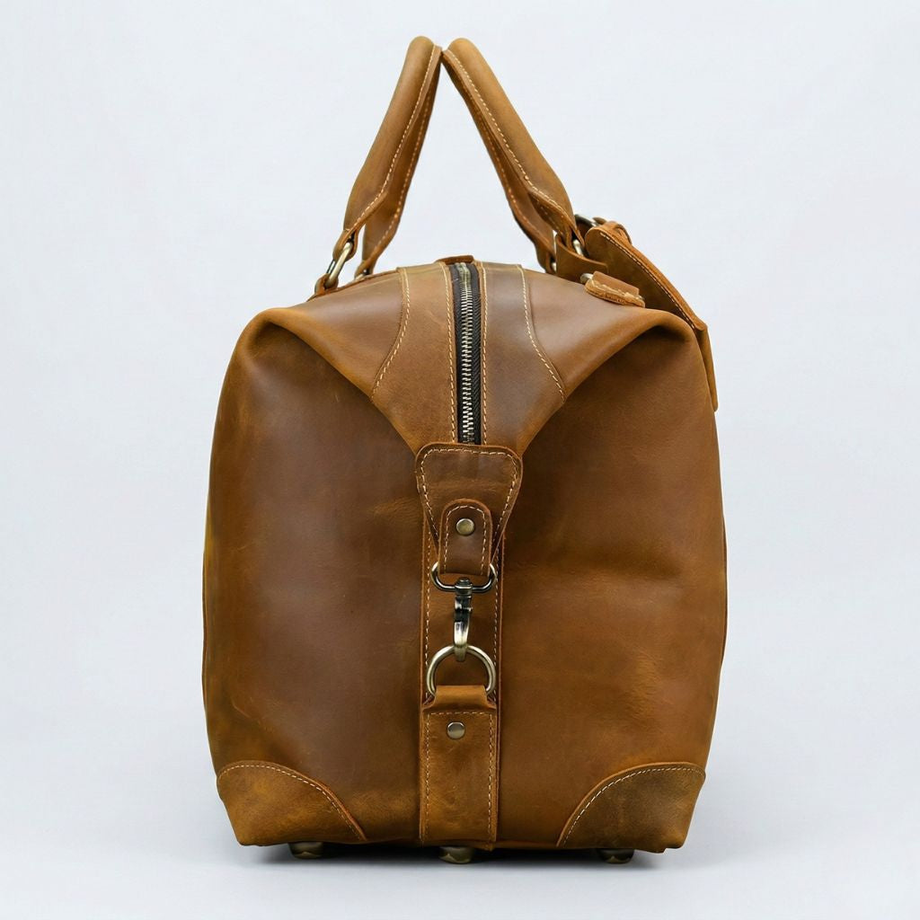 Profil droit du sac de voyage cuir cognac, fermeture à glissière verticale et crochet de bandoulière laiton