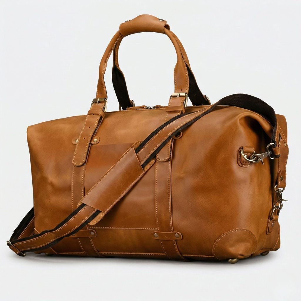 Sac de voyage en cuir caramel huilé, vue trois-quarts, poignée matelassée, poche frontale et bandoulière textile