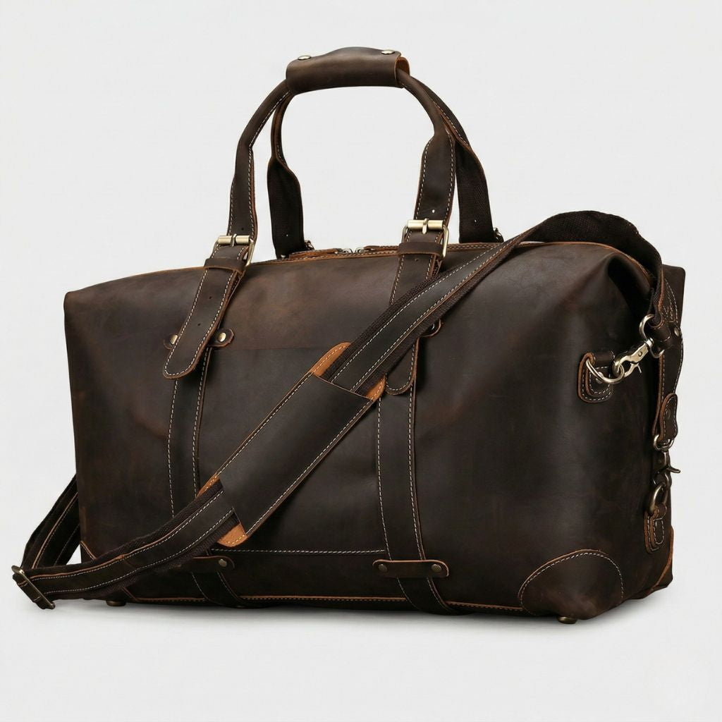 Sac de voyage en cuir chocolat foncé, vue trois-quarts, poignée plate, liserés cognac sur la poche frontale