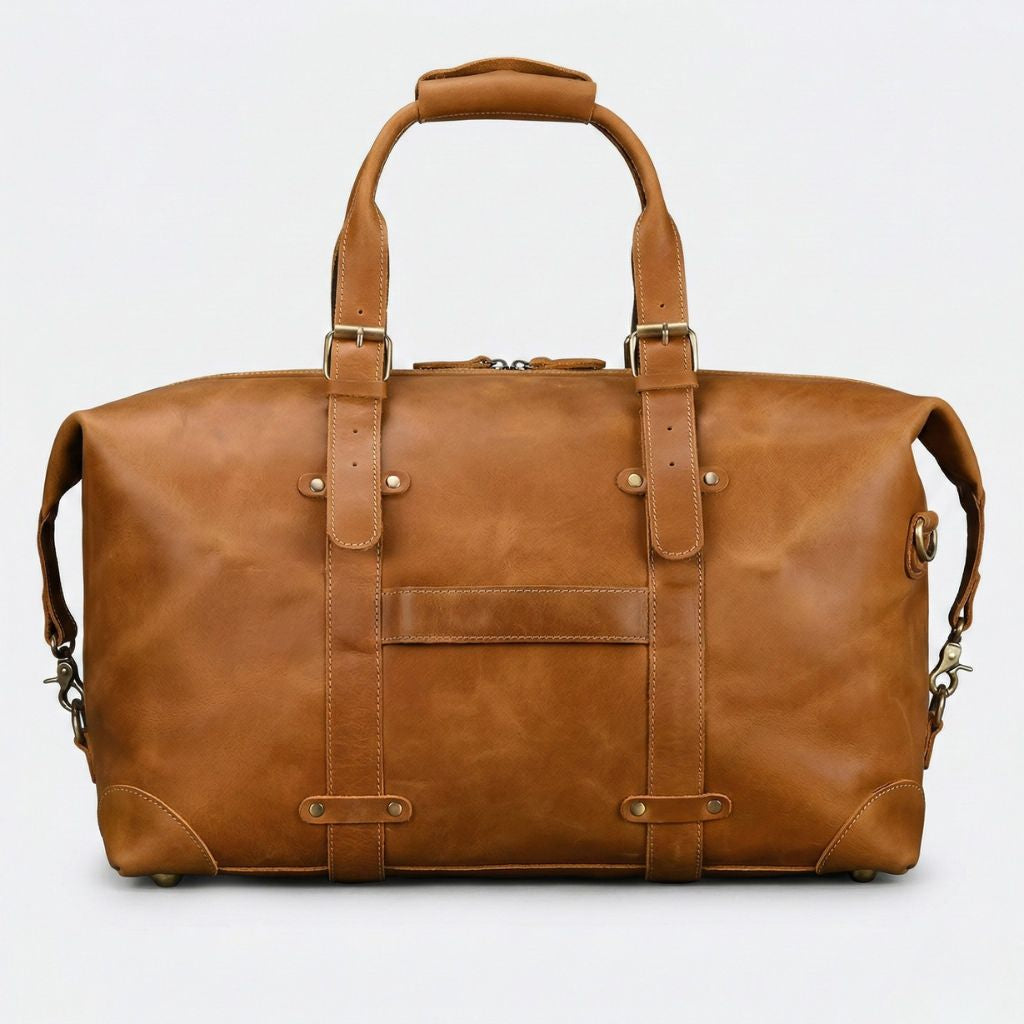 Face avant du sac de voyage cuir cognac tanné, poche plate centrale, bretelles rivées et fermeture zip laiton
