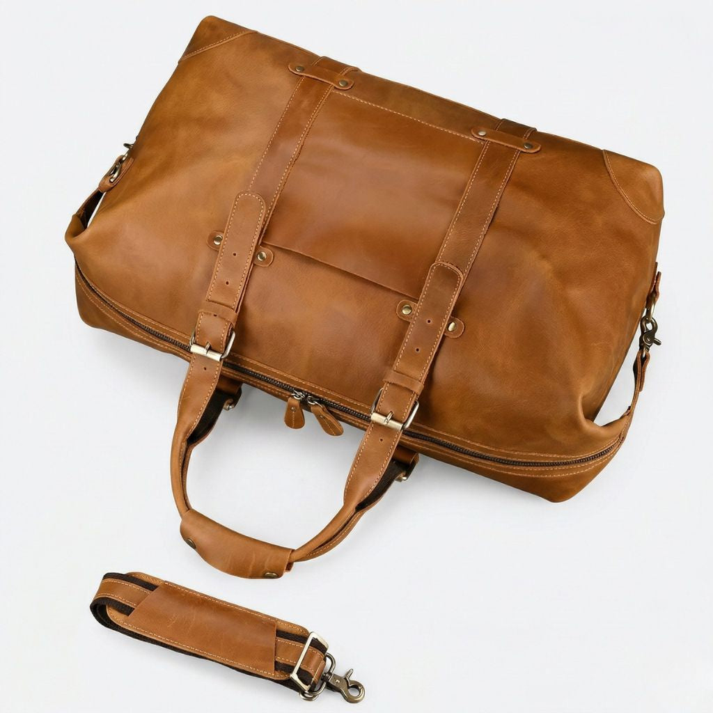 Vue plongeante du sac de voyage cognac, dessus et poche frontale visibles, bandoulière canvas détachée à côté