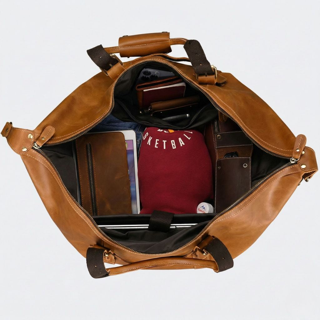 Vue du dessus d'un sac de voyage en cuir camel ouvert, rempli d'un ordinateur, carnets, vêtements et portefeuille Image