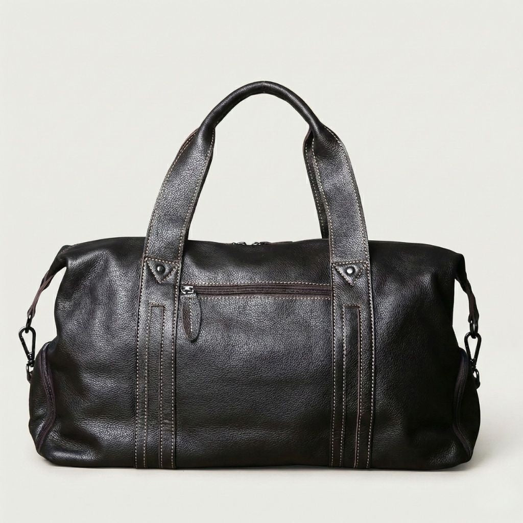 Dos du sac de voyage en cuir grainé noir, poche zippée avant visible, bandoulière et fermetures latérales