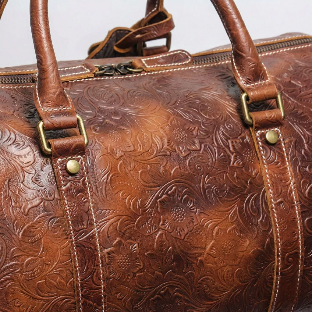 Gros plan sur le cuir embossé motifs floraux marron cognac, ferrures laiton et poignées du sac cabine
