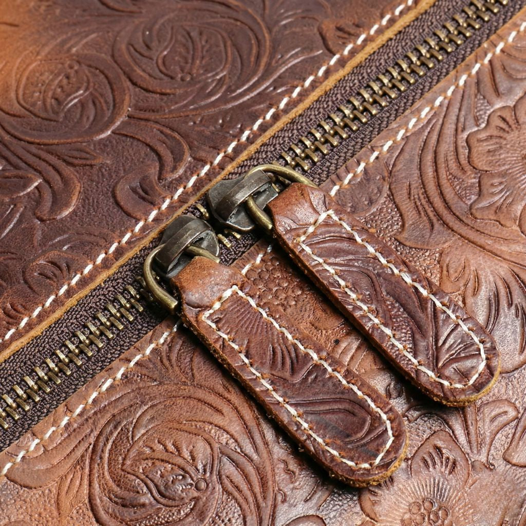 Gros plan sur la double fermeture éclair en laiton bronze du sac de voyage cuir brun, coutures blanches apparentes