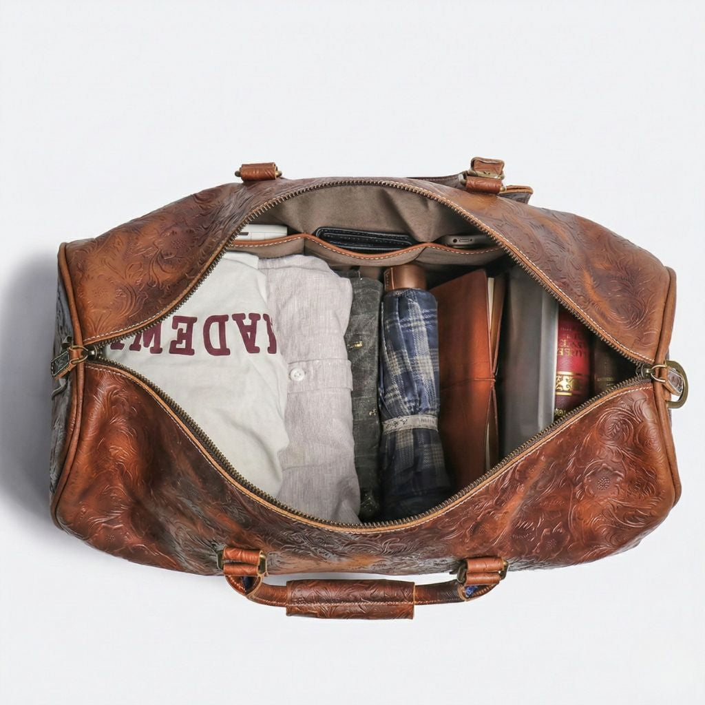 Vue de dessus du sac de voyage en cuir marron embossé ouvert, contenant chemise, jean, parapluie et livre Image