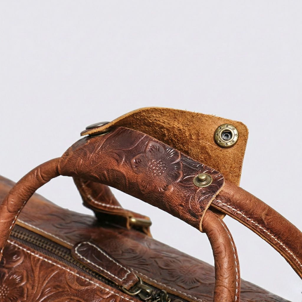 Détail de l'étiquette bagage en cuir embossé floral avec bouton-pression et des poignées rondes en cuir marron