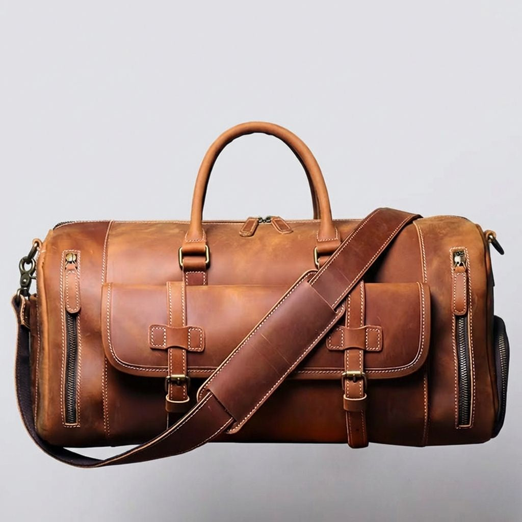 Face avant du sac de voyage cuir cognac, poche à rabat avec sangles à boucles et deux poches latérales