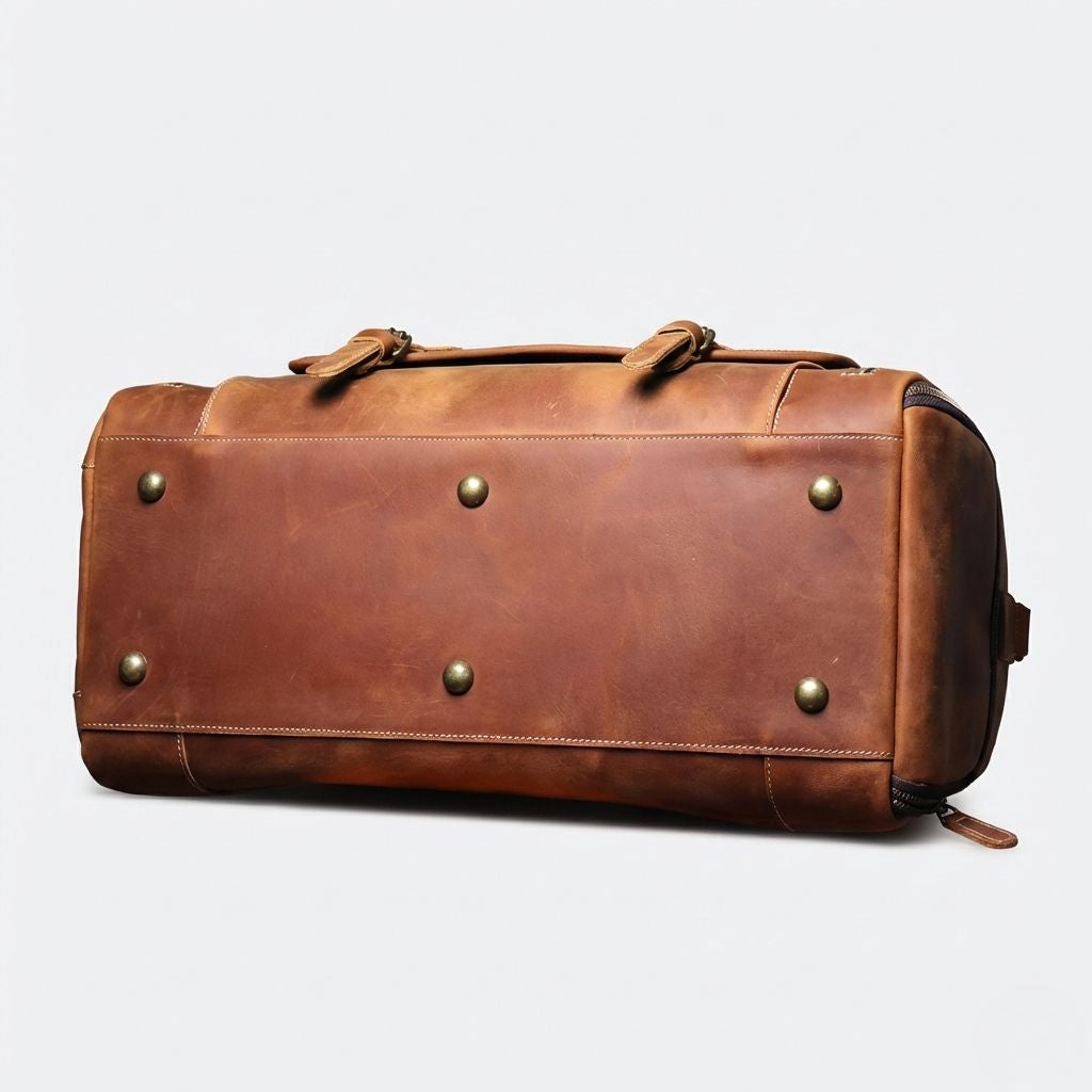Dessous du sac de voyage cuir cognac couché sur le côté, six pieds protecteurs en bronze vieilli