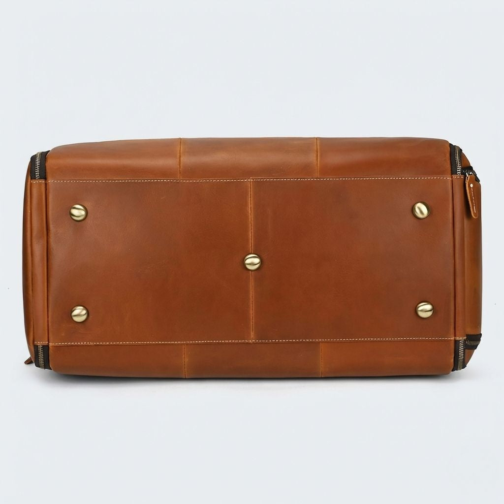 Dessous du sac de voyage en cuir cognac, cinq pieds protecteurs dorés sur panneaux assemblés