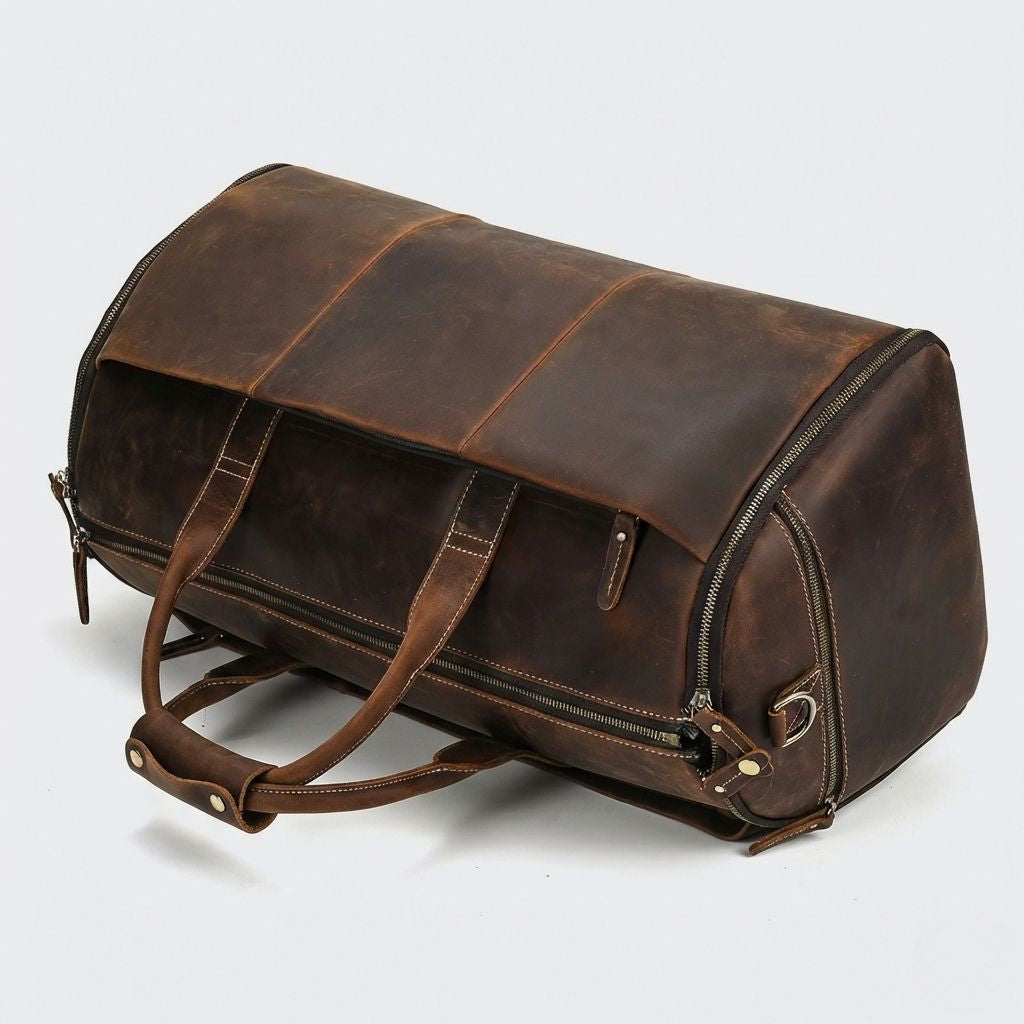 Sac de voyage en cuir brun posé sur le côté, poignées apparentes et anneau D en laiton vieilli