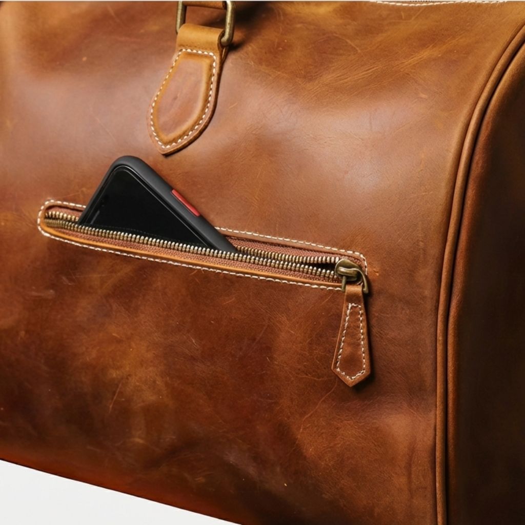 Poche frontale du sac de voyage cuir cognac ouverte avec un smartphone, zip bronze à languette cuir