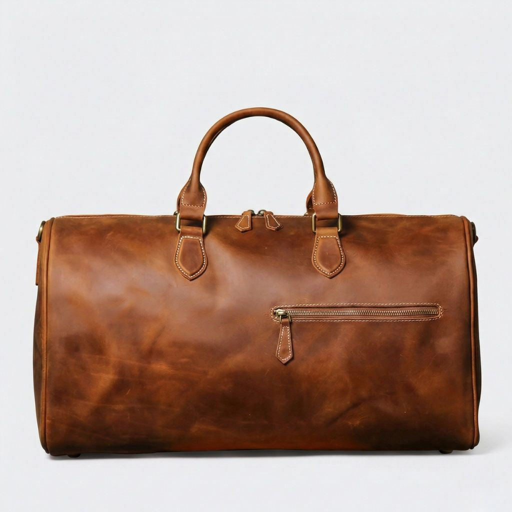Face avant du sac de voyage cabine cuir cognac, poche zippée horizontale et double tirette en laiton