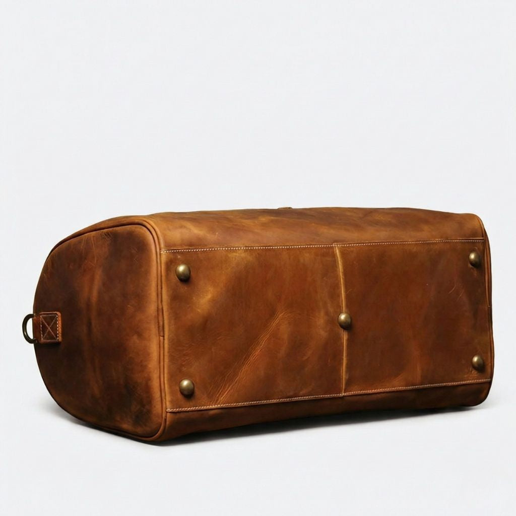 Dessous du sac de voyage en cuir cognac posé sur le côté, pieds protecteurs en bronze vieilli