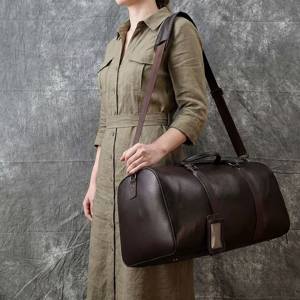 Femme portant le sac cabine marron en cuir grainé en bandoulière sur fond textile gris ardoise