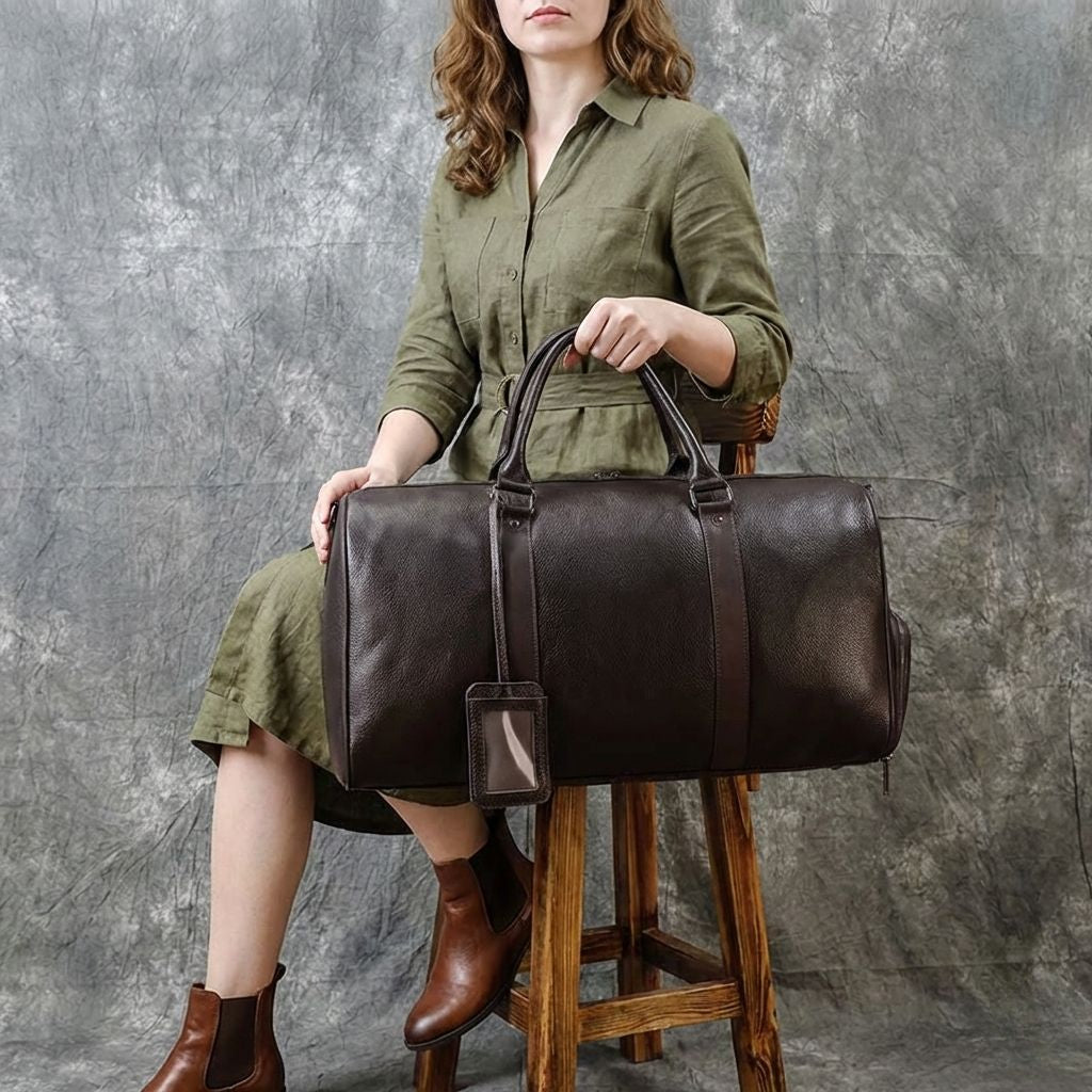 Femme en robe verte assise tenant un grand sac de voyage femme en cuir marron foncé avec poignées courtes Image