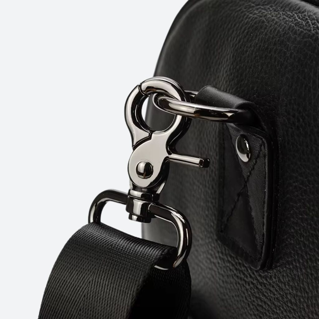 Gros plan du mousqueton argenté de la bandoulière du sac de voyage cuir grainé noir et son anneau D