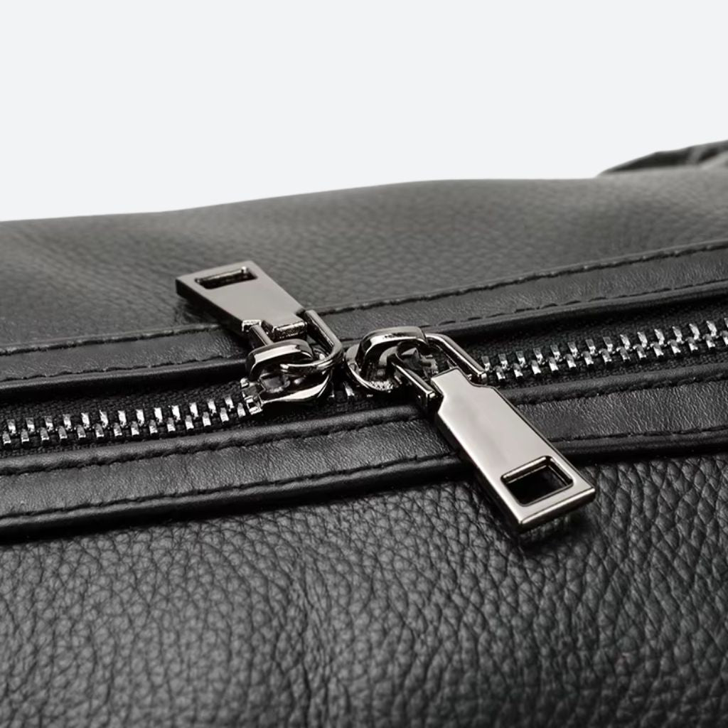 Gros plan de la double tirette de fermeture éclair du sac de voyage cuir grainé noir, quincaillerie gunmetal