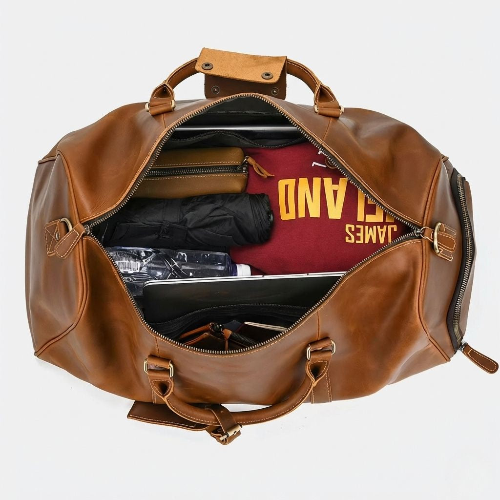 Intérieur du sac de voyage cognac ouvert, vue du dessus avec laptop, vêtements et bouteille d'eau