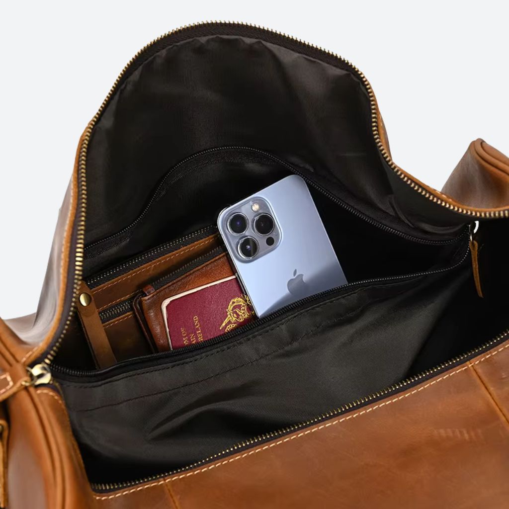 Gros plan de la poche intérieure du sac cognac avec smartphone, passeport et portefeuille visibles