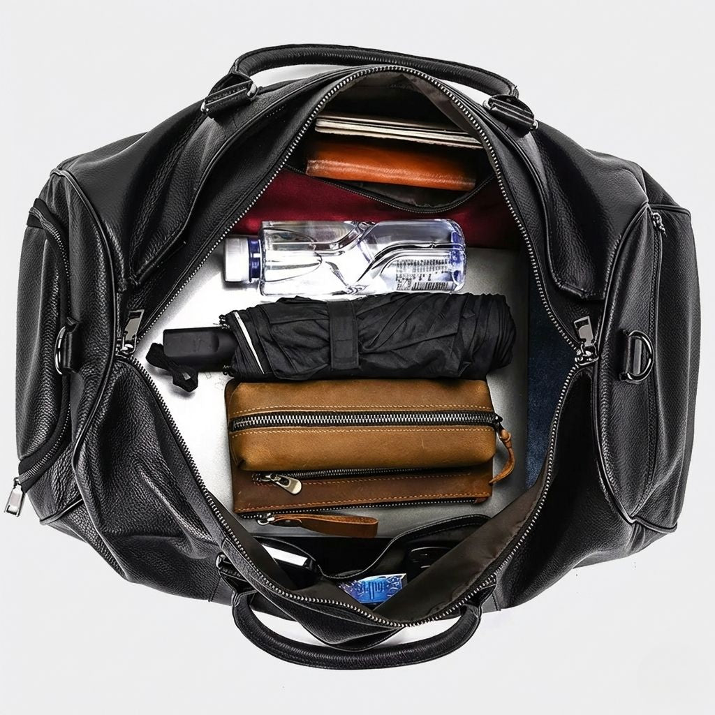 Intérieur du sac de voyage noir ouvert, vue du dessus avec bouteille, parapluie, portefeuille et trousse