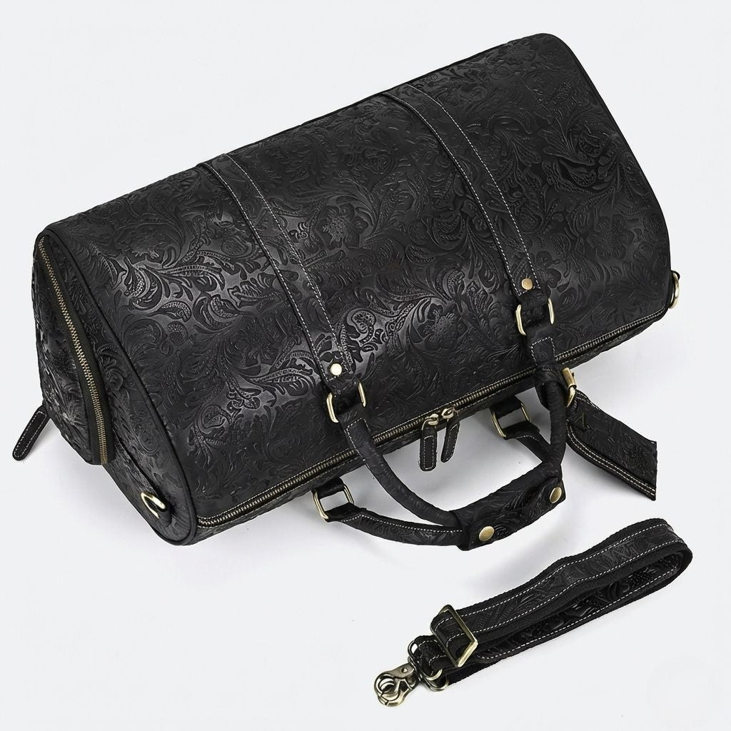 Vue de côté du sac de voyage cuir noir embossé floral couché, bandoulière et ferrures en laiton bronze visibles