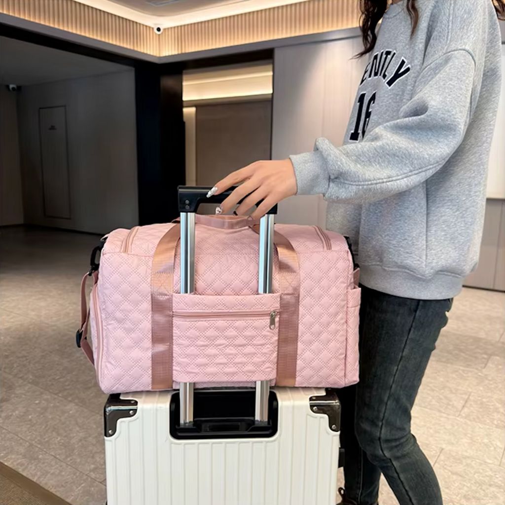 Femme posant un sac de voyage matelassé rose poudré sur une valise blanche dans un hall d'aéroport Image