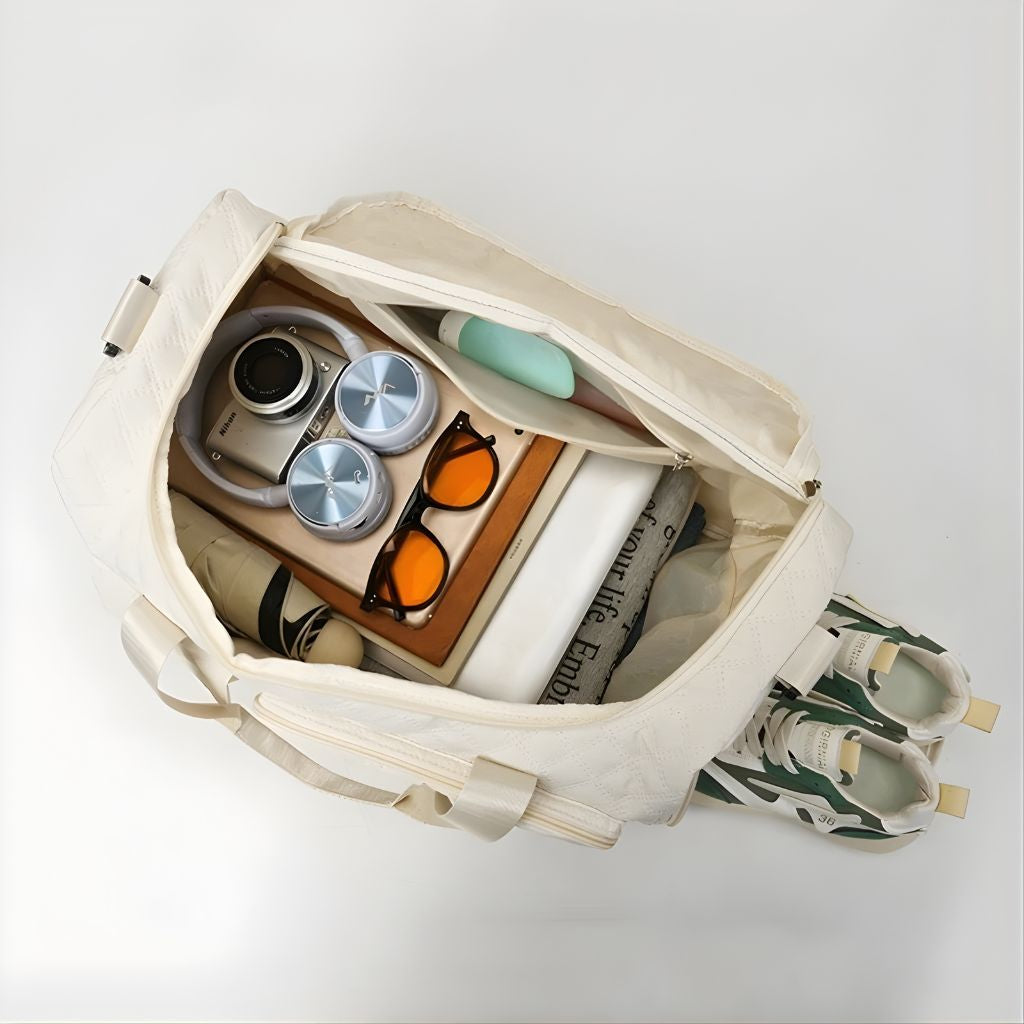 Vue plongeante du sac de voyage femme blanc cassé ouvert, appareil photo, casque, lunettes et chaussures rangés