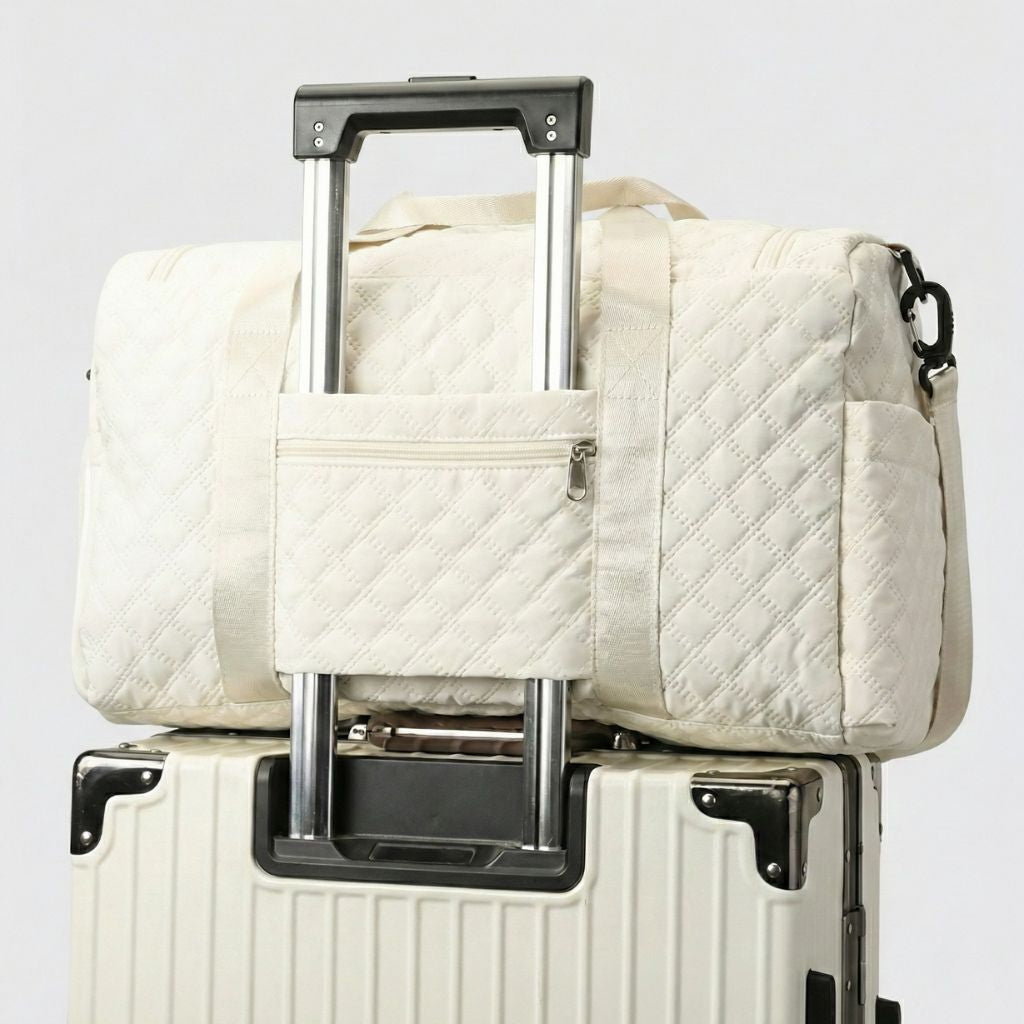 Sac de voyage femme cabine matelassé blanc cassé glissé sur la poignée télescopique d'une valise à roulettes