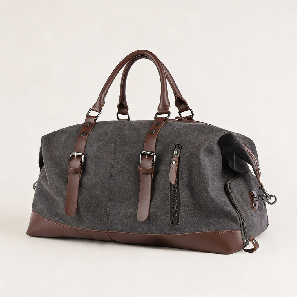 Sac de voyage toile canvas gris anthracite, vue 3/4, renforts, poignées cuir brun, sangles boucles et poche zippée