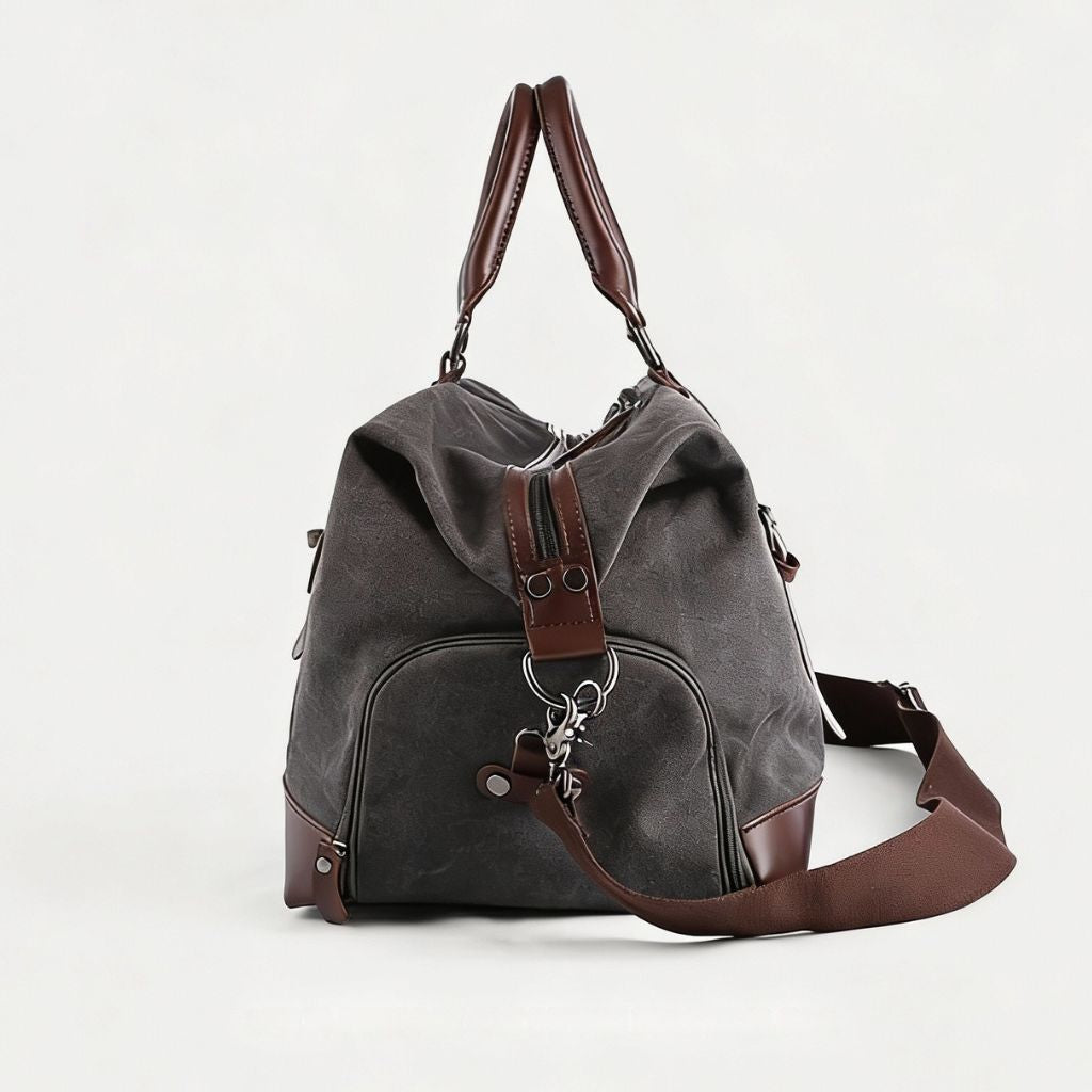 Sac de voyage toile canvas gris anthracite vu de profil, renforts cuir brun, poche arrière zippée et breloque