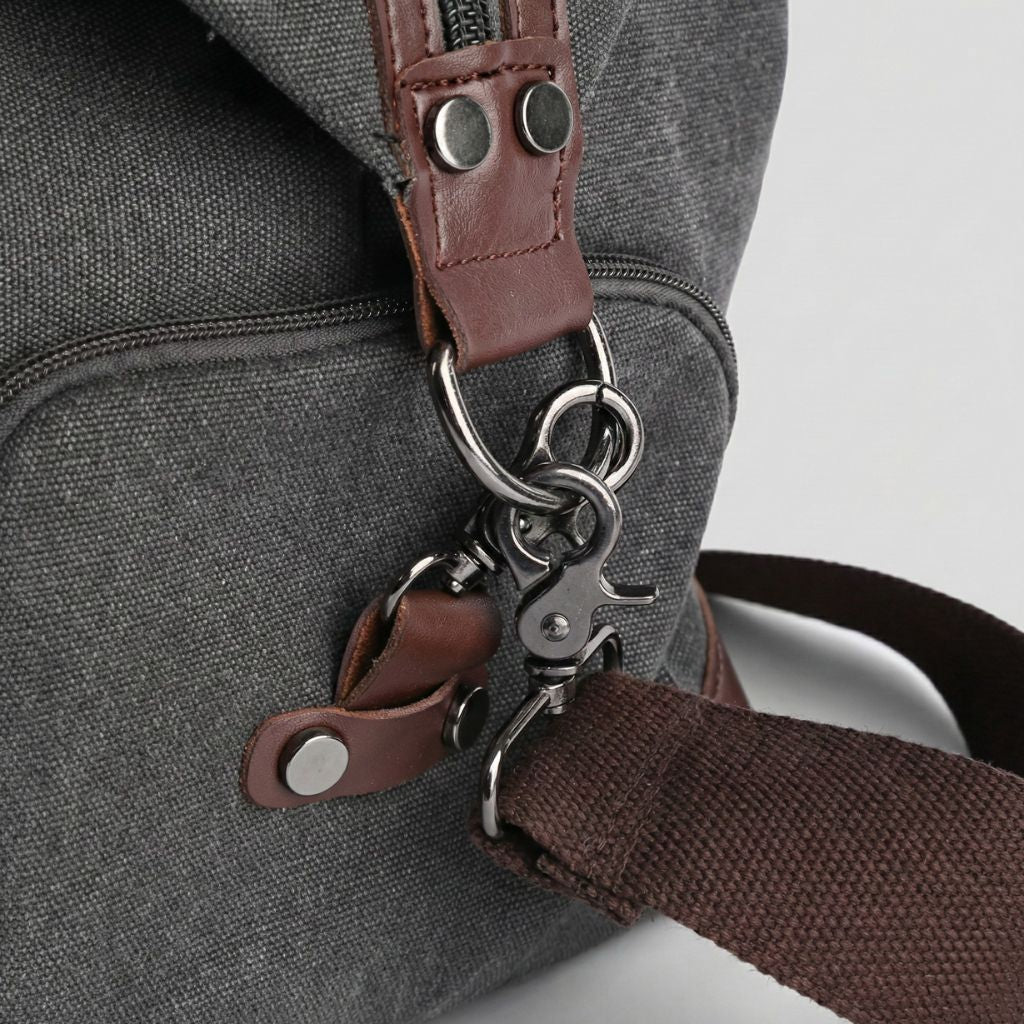 Gros plan sur les fermoirs dorés et la bandoulière amovible d'un sac de voyage en canvas gris foncé Image