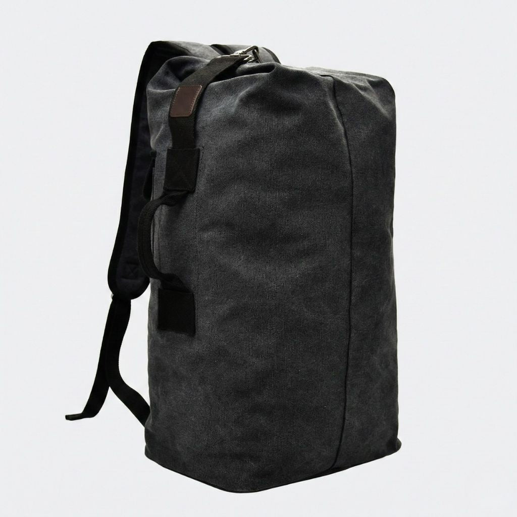 Sac de voyage en canvas noir, forme cylindrique haute avec bretelles dos et patch en cuir foncé sur la poignée