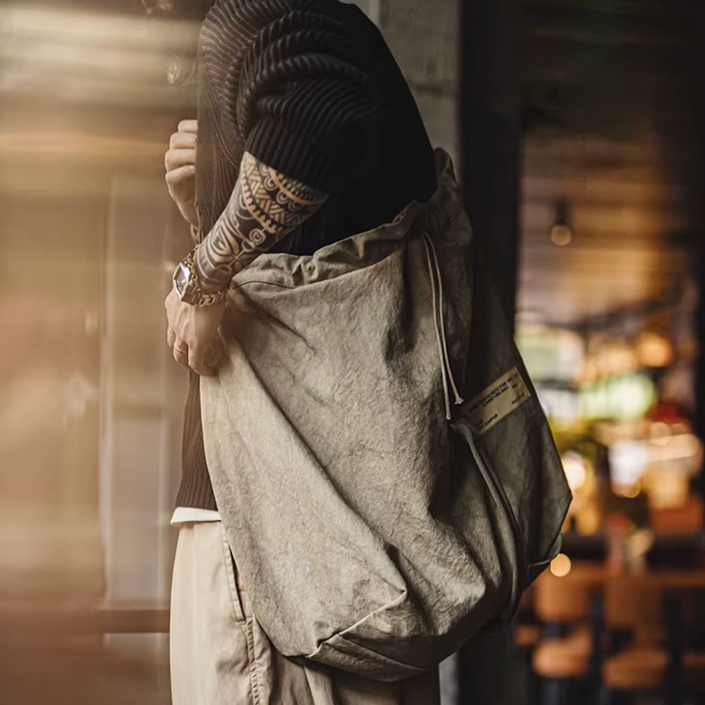 Homme de profil portant en bandoulière un sac de voyage en toile militaire kaki, look urbain vintage décontracté