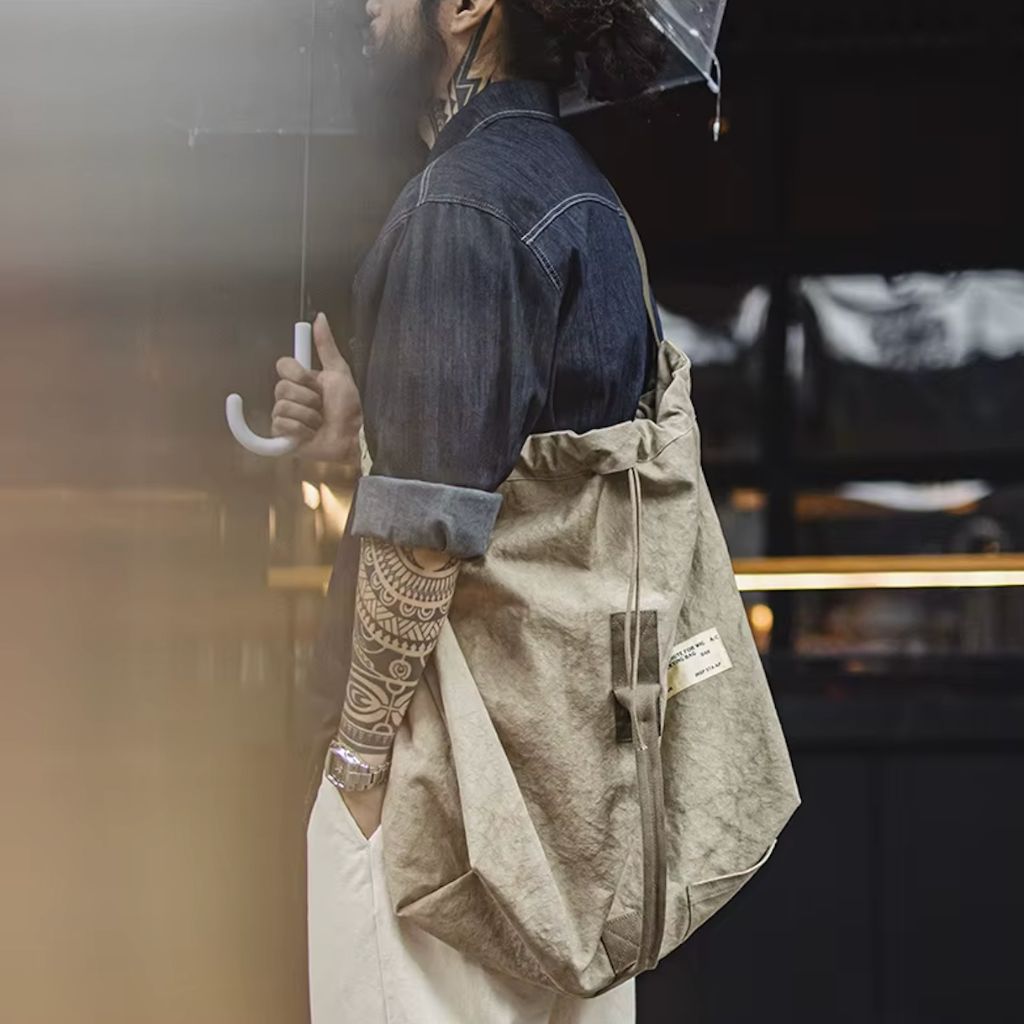 Homme sous la pluie portant un sac de voyage en toile militaire kaki en bandoulière, imperméable style urbain