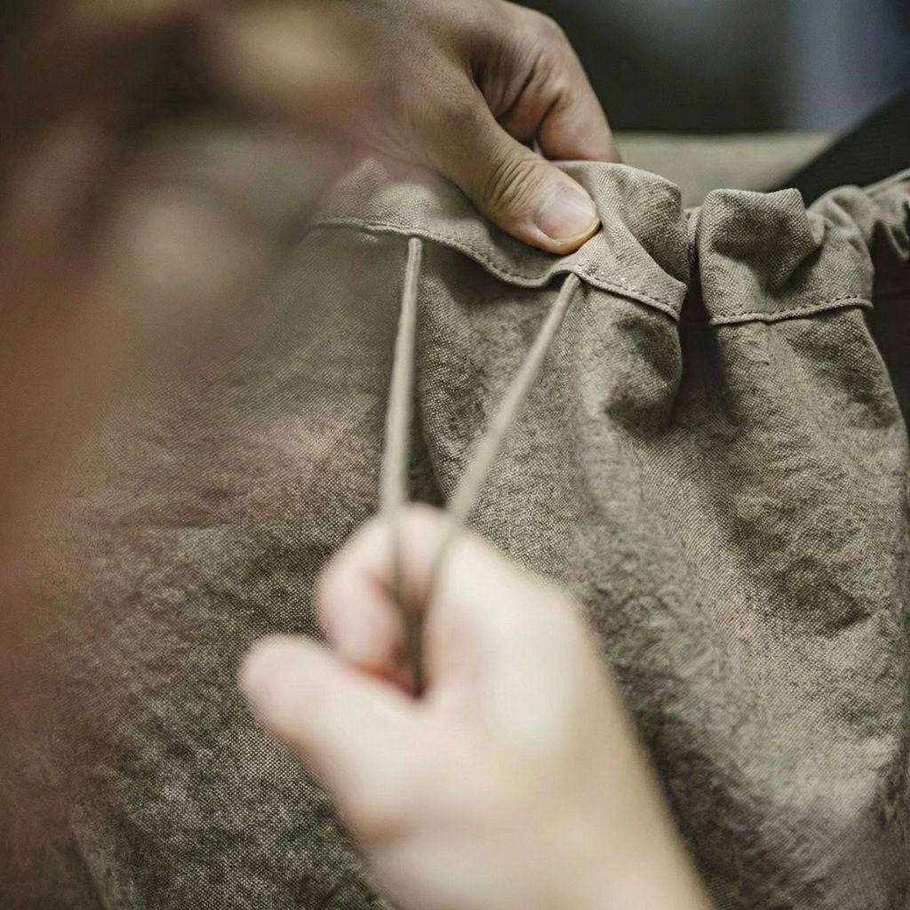 Détail de la fermeture en cordon du sac de voyage en toile militaire kaki, mains resserrant le cordon supérieur