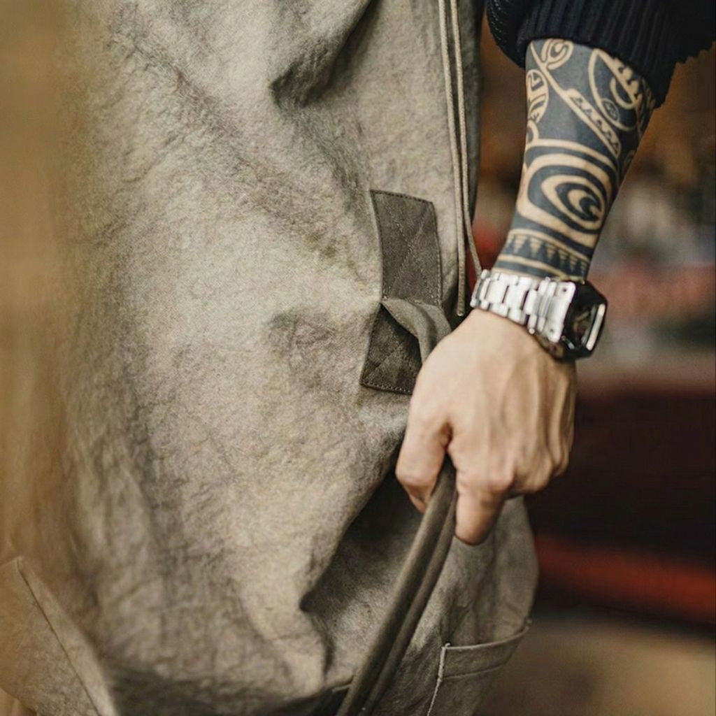 Homme tatoué portant à la main un grand sac de voyage en toile canvas kaki vintage avec bandoulière Image